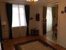 бежевый с коричневым ковер на полу светлой гостиной с торшером и коричневым квадратным столиком в углах комнаты с прозрачной гардиной и синими шторами на окнах кв 27