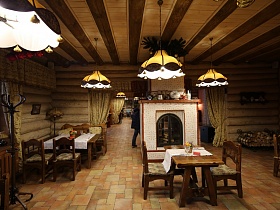 столы и стулья из натурального дерева в отдельных зонированных комнатах с желтыми шторами на дверных проемах из бревен ресторана в древне русском стиле