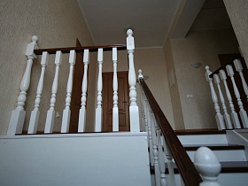 белые перила лестничной площадки второго этажа с входными дверьми в комнаты кирпичного двухэтажного дома