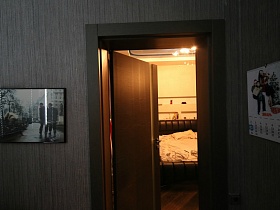 картина и календарь на серых стенах просторной лоджии с открытой дверью в спальную комнату квартиры студии молодежной семьи