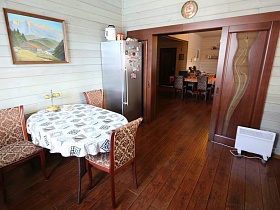 картина на стене над обеденным столом, серебристый холодильник у раздвижных деревянных межкомнатных дверей современного деревянного дома