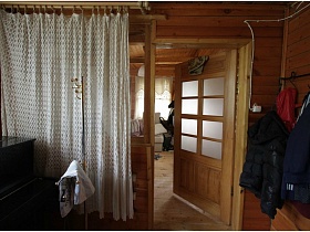 настенная вешалка с вещами,белая гардина на окне у межкомнатной двери на деревянной даче музыканта