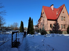 деревянная скамейка под крышей вдоль расчищенной дорожки от снега на участке загородного дома