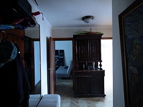картина на стене напротив мебельной стенки и коричневый шкаф у стены светлой прихожей стильной квартиры художника в сталинке