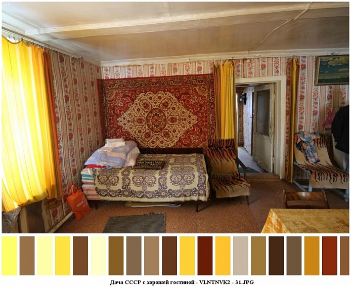 большая двух спальная кровать с деревянной спинкой и двумя матрасами под покрывалом у стены с красным ковром и креслами у входной двери