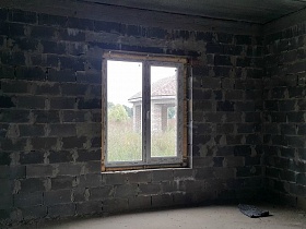 стена из шлакоблока с пластиковым окном в недостроенном доме коттеджного поселка на берегу реки