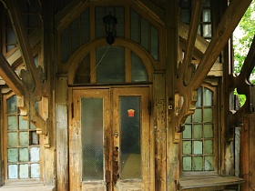 черный уличный фонарь над арочным окном и деревянной дверью со стеклянными вставками под навесом на резных опорах старинного деревянного дома в старом Ногинске