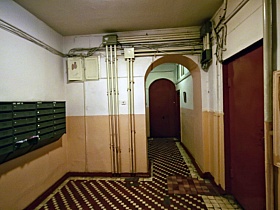 ряд зеленых почтовых ящиков на стене просторного холла  первого этажа с арочным дверным проемом к входным дверям квартиры в сталинском доме