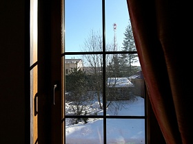 вид на участок под снегом через рамочное окно кабинета загородного деревянного дома с камином