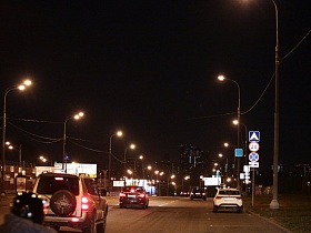 оживленная автомобильная дорога под ярким освещением фонарных столбов с многочисленными дорожными знаками в ночное время