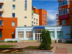 белое одноэтажное здание с высоким цоколем и лестницей стоматологии между двумя разноцветными домами