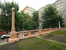 окрашенный в персиковый цвет бетонный резной забор с освещением на столбах  у сталинского дома