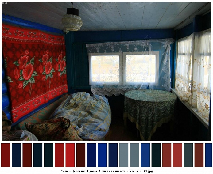 незаправленный диван у синей деревянной стены с плюшевым красным ковром, круглый стол покрытый скатертью у окон веранды с белыми гардинами жилого дома в деревне