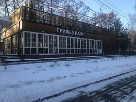 деревянные перила просторной открытой террасы на крыше кафе-стекляшки вдоль зимней автомобильной дороги в лесополосе