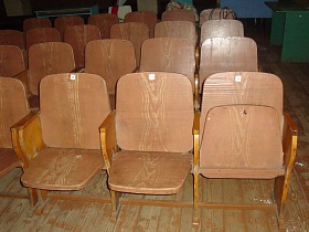коричневые деревянные секционные кресла на деревянном полу со старой краской актового зала клуба эпохи СССР