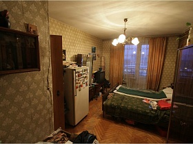 белый холодильник, трюмо, две деревянные односпальные кровати,люстра с белыми плафонами на потолке спальной комнаты с песочными шторами на окне квартиры эпохи СССР
