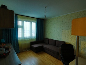 коричневый мягкий угловой диван у окна с синими шторами на окне рабочей комнате большой трехкомнатной квартиры в переезде