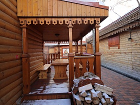 заготовленные поленья у открытой веранды под крышей с деревянным столом и скамейкой