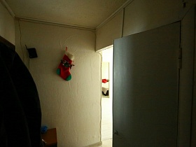 настенная вешалка с одеждой и новогодний сапожок на стене прихожей съемной квартиры на первом этажея