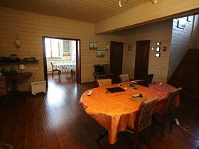пестрые стулья со спинками у стола с ораньжевой скатертью, стулья и круглый журнальный столик у стены просторной гостиной деревянного трехэтажного дома