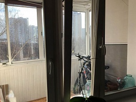 вид на большой зашитый и застекленный просторный балкон двухкомнатной современной квартиры из окна гостиной