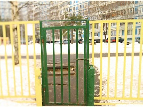 зеленые ворота в желтом металлическом заборе вокруг детского садика