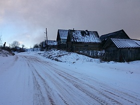 широкая заснеженная улица в заброшенной деревне со старыми деревянными домами