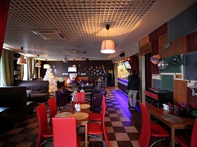 коричневая центральная стена с телевизором и различной спортивной атрибутикой в просторном зале кафе-бара с рядами уютных столиков для отдыха