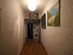 большие картины на светлых стенах длинной прихожей  с коричневым линолеумом на полу красивой лофт квартиры художника