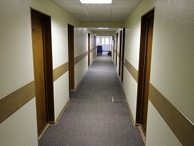 двери в номера гостиницы в длинном коридоре с серым ковровым покрытием на полу