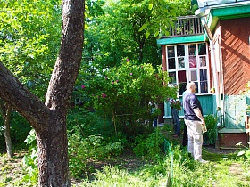 открытый балкон с перилами над верандой деревянной художественной дачи-музей с цветущим зеленым участком за зеленым забором