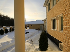 вид с крыльца светлого загородного дома на двор в снегу и расчищенную дорожку к гаражу