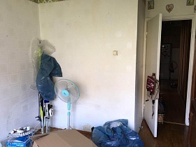 напольный вентилятор, коробки и голубые пакеты с вещами на полу комнаты с белыми стенами после ремонта квартиры в Бибирево