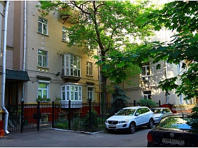 черный высокий металлический забор вокруг полисадника с лиственными и хвойными деревьями у дома на Долгоруковской