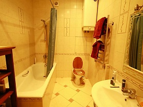 белая ванна, зашитая плиткой за зеленой шторкой, санузел, зеркало в рамке над белой раковиной в ванной комнате с бежевой плиткой на стенах трехкомнатной квартиры в жилом доме