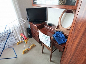 телевизор на комоде, гримерный столик с зеркалом, сушилка для белья и детская качелька в спальне семейной трешки