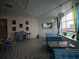 фотографии на белых стенах, плоский телевизор, мягкие голубые диванчики вокруг стола у больших окон светлого зала Бар Лофта в спальном районе