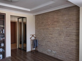 коричневая напольная вешалка для одежды у кирпичной стены в гостиной с белым потолком семейной трехкомнатной квартиры с дизайнерским ремонтом