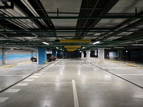 ровные ряды с отмеченными парковочными местами между цветными колоннами в просторном цветном современном паркинге с подвесным шлагбаумом под потолком