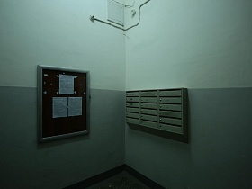 доска объявлений, серые почтовые ящики на стене подъезда 4 с серыми панелями и серым полом в жилом доме эпохи СССР