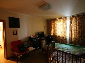 телевизор на светлом комоде, большой комод, красное кресло и детский стульчик у стены спальной комнате двушки в новосторойке