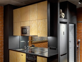 бежевая с коричневым кухня у серой стены из гипсокартона, на углу ванной комнаты с открытой дверью стильной студии в стиле хай тек