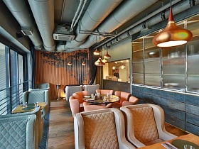 оранжевая рифленая декорированная ширма в конце узкого зала с серыми, коричневыми и бежевыми креслами у сервированных столиков ресторана лофт