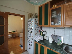 белый холодильник с многочисленными магнитиками у коричневой кухни с зелеными дверцами в простой квартире на Садовом