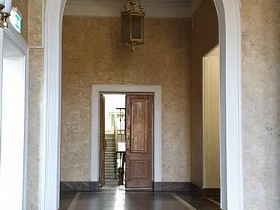 ступени на входе в просторный классический подъезд с арочным дверным проемом, белыми колоннами,высокими бежевыми стенами сталинского высотного жилого дома советской эпохи