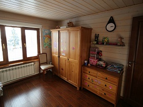 деревянный трехдверный шкаф для одежды,часы над полочкой на стене и деревянный комод у стены спальной комнаты просторного трехэтажного дома