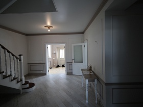 просторный светлый вестибюль с деревянной лестницей, столиком на паркетном полу и открытой дверью в прихожую с обувью у входной двери