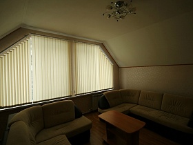 белая люстра над журнальным столом в комнате отдыха с угловыми диванами на мансарде двухэтажного съемного дома в сосновом лесу