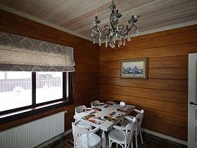 белые стулья со спинками у белого раздвижного стола с цветными салфетками в кухне современного деревянного съемного коттежда