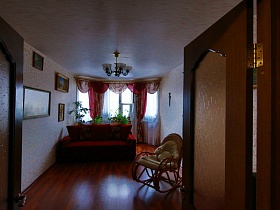 открытые деревянные двери с рефленным стеклом в светлую гостиную с красным диваном с мягкими подушками и креслом качалкой